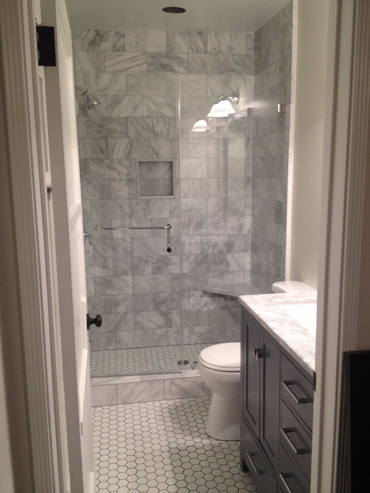 Bathroom with marble tile shower, toilet, gray vanity with white countertop, and white and gray floor tile.