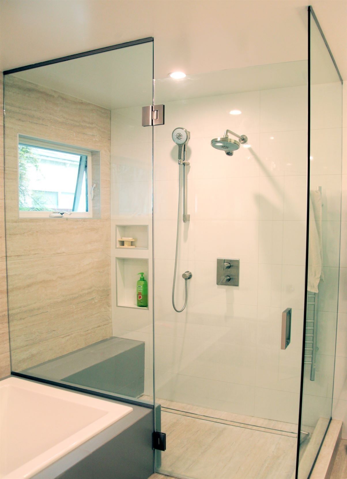 Modern glass shower enclosure in bathroom with built-in bench, neutral tile, and shower fixtures.