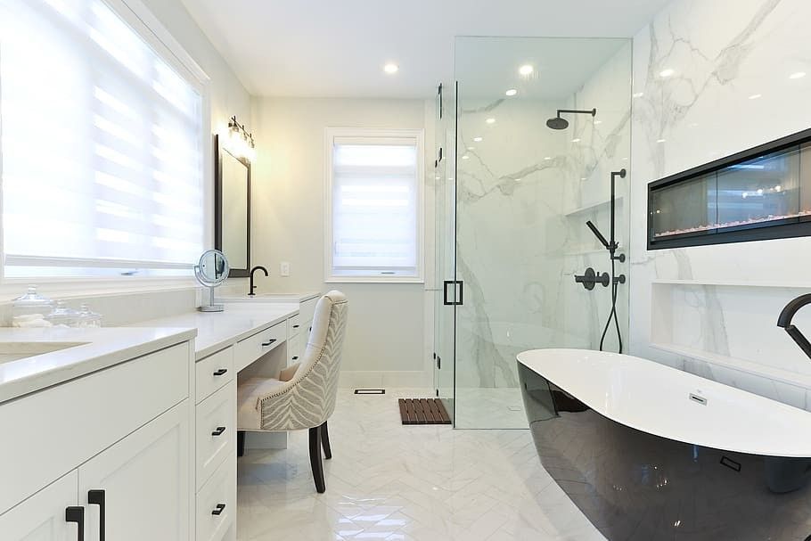 Modern white bathroom with black accents: vanity, glass shower, bathtub, fireplace, and window.