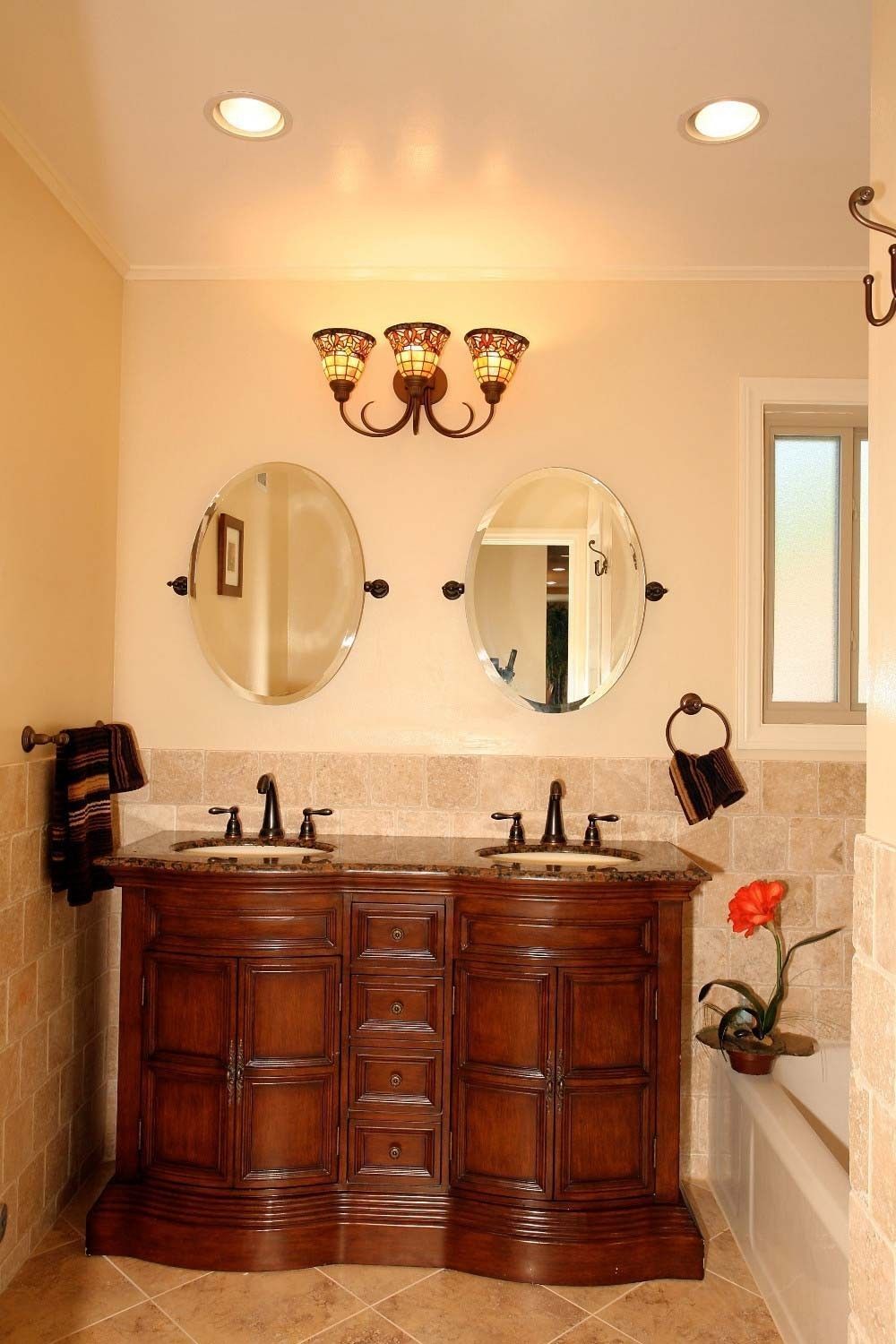 Bathroom with double vanity, oval mirrors, and warm lighting.