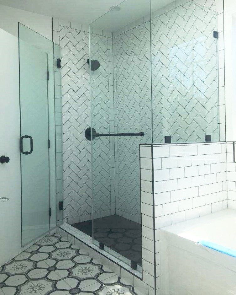 Glass shower enclosure with white and black tile, black fixtures, and patterned floor.