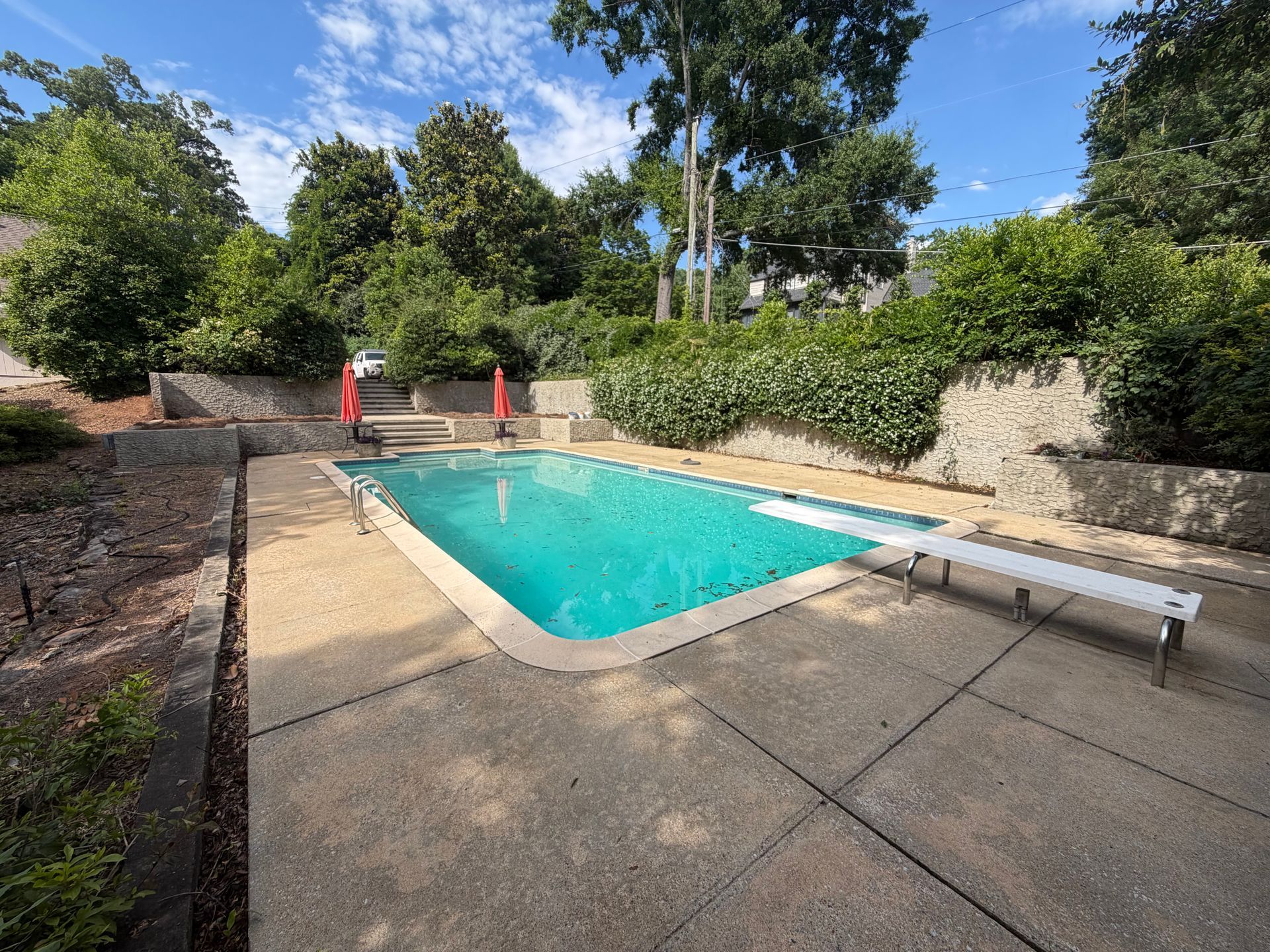 Backyard swimming pool with stone deck, lounge chair, and lush greenery under a blue sky