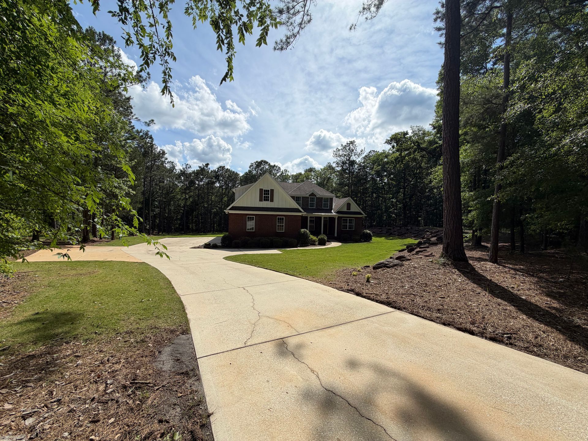 Curved driveway leading to a house surrounded by trees on a sunny day