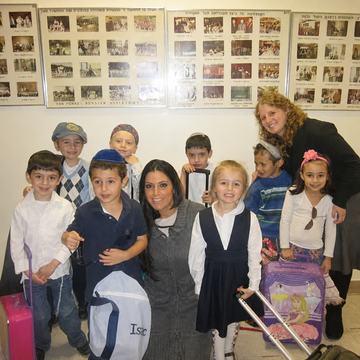 Group of children with a woman posing indoors in front of a photo display wall.