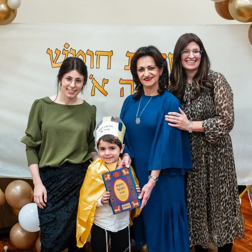 Three women and a child posing at a festive event with balloons and Hebrew decorations
