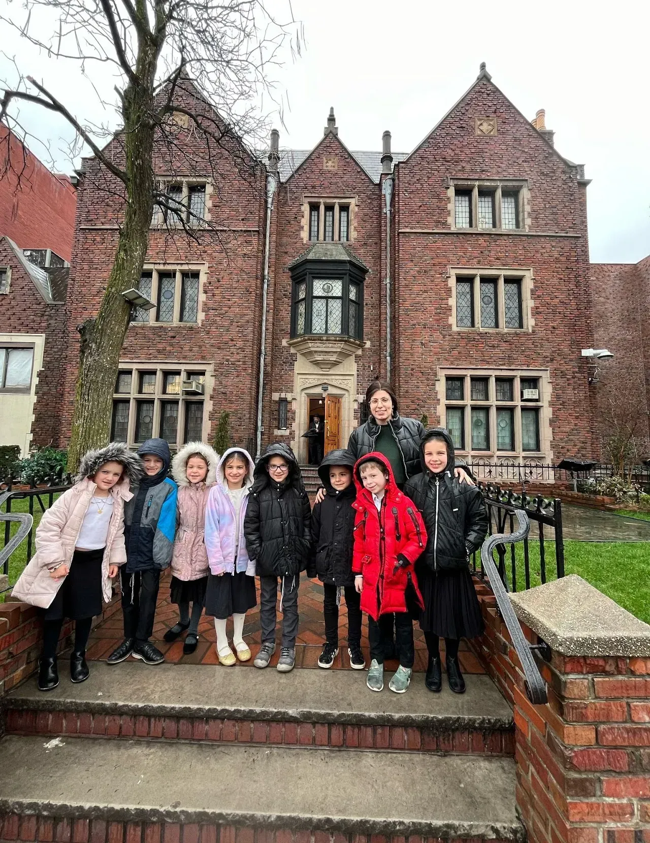 Group of people posing on steps in front of a red-brick historic building on a rainy day