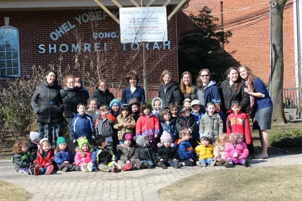 Group of children and adults posing outside a brick building with a “Shorei Torah” sign.