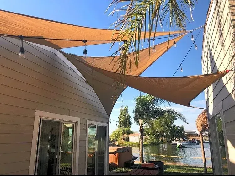 Patio with tan shade sails, white building, and canal view under a blue sky