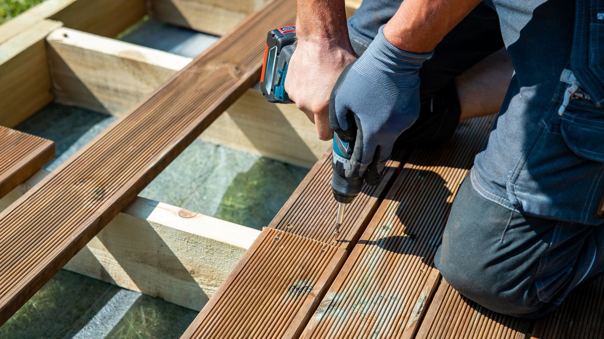 A man is using a drill on a wooden deck.