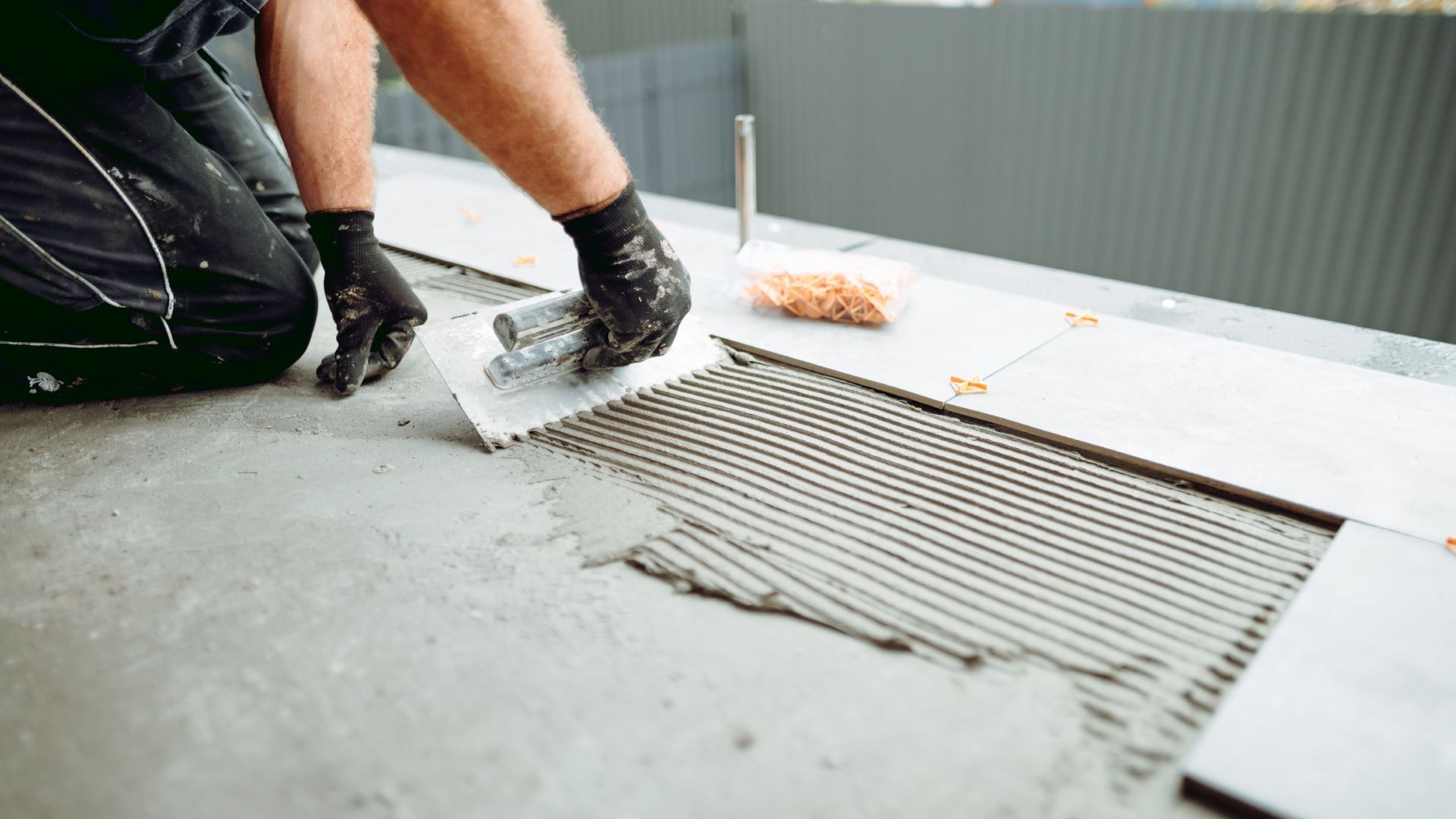 A man is laying tiles on the floor with a trowel.