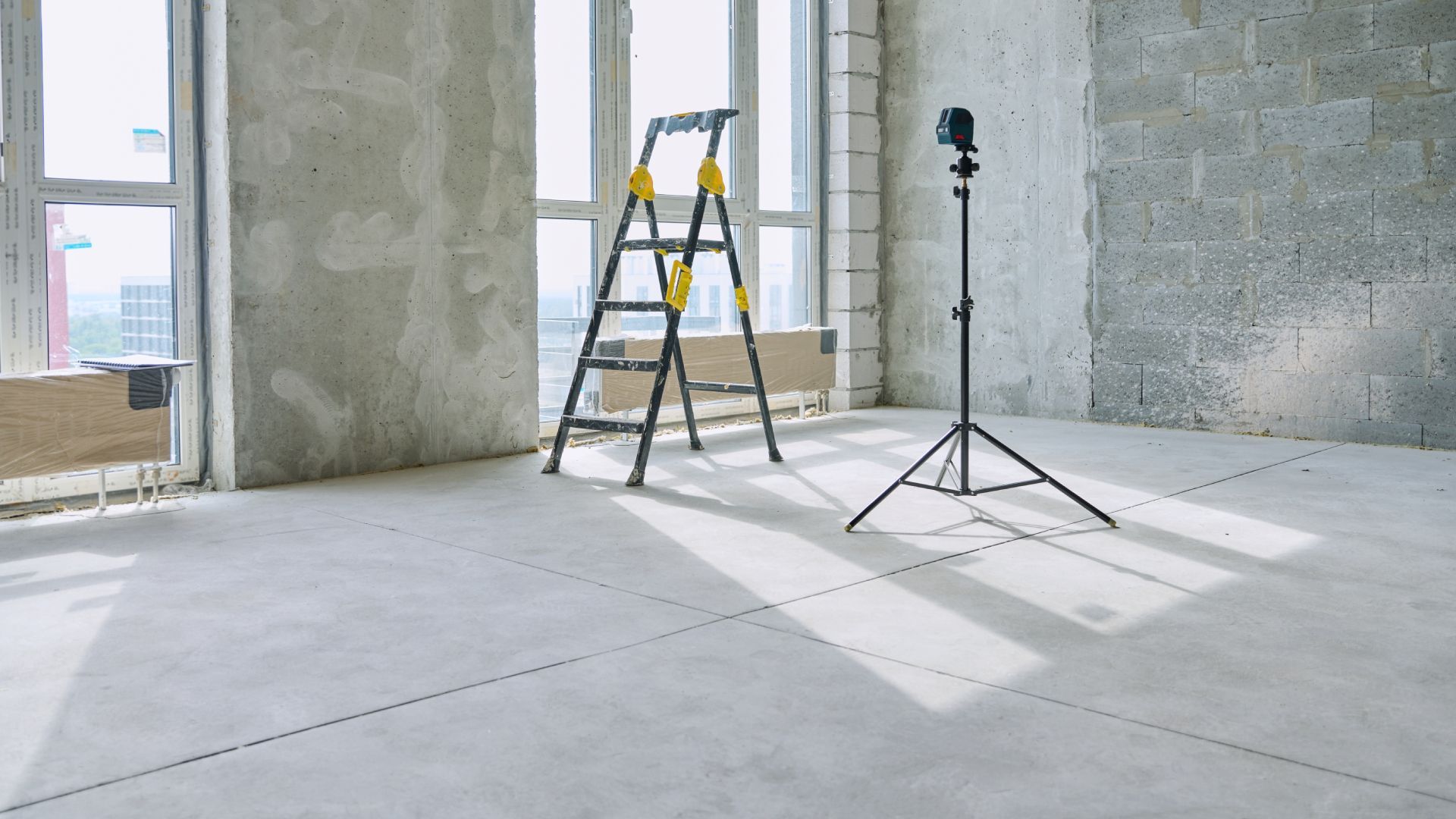 An empty room with a ladder and a tripod in it.