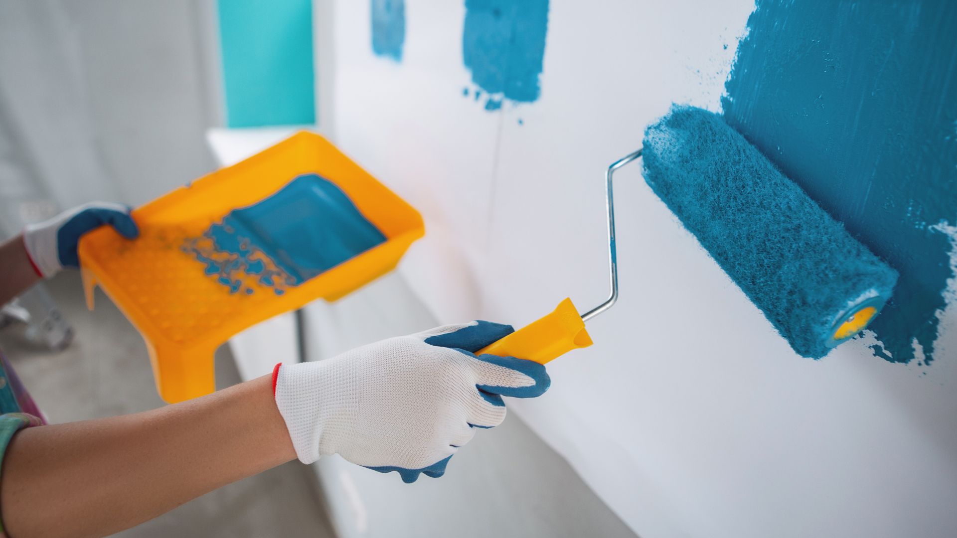 A person is painting a wall with a blue paint roller.