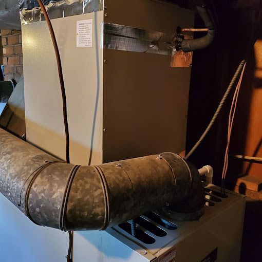 A dirty pipe is attached to a heater in a basement.