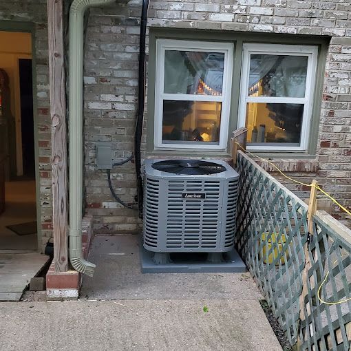 An air conditioner is sitting outside of a brick house next to a window.