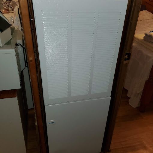 A white refrigerator is sitting in a room next to a door.