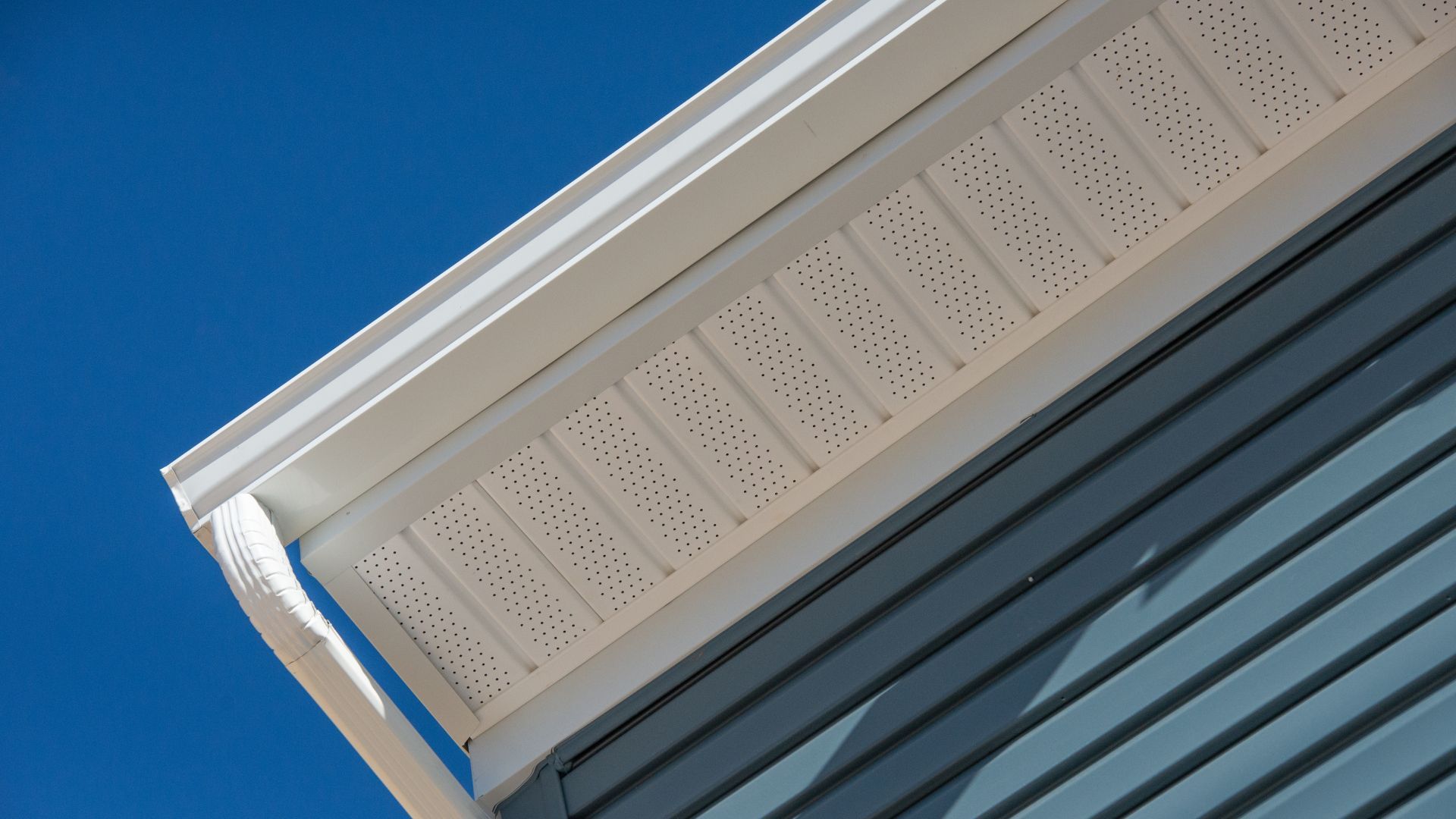 A white gutter on a blue house with a blue sky in the background