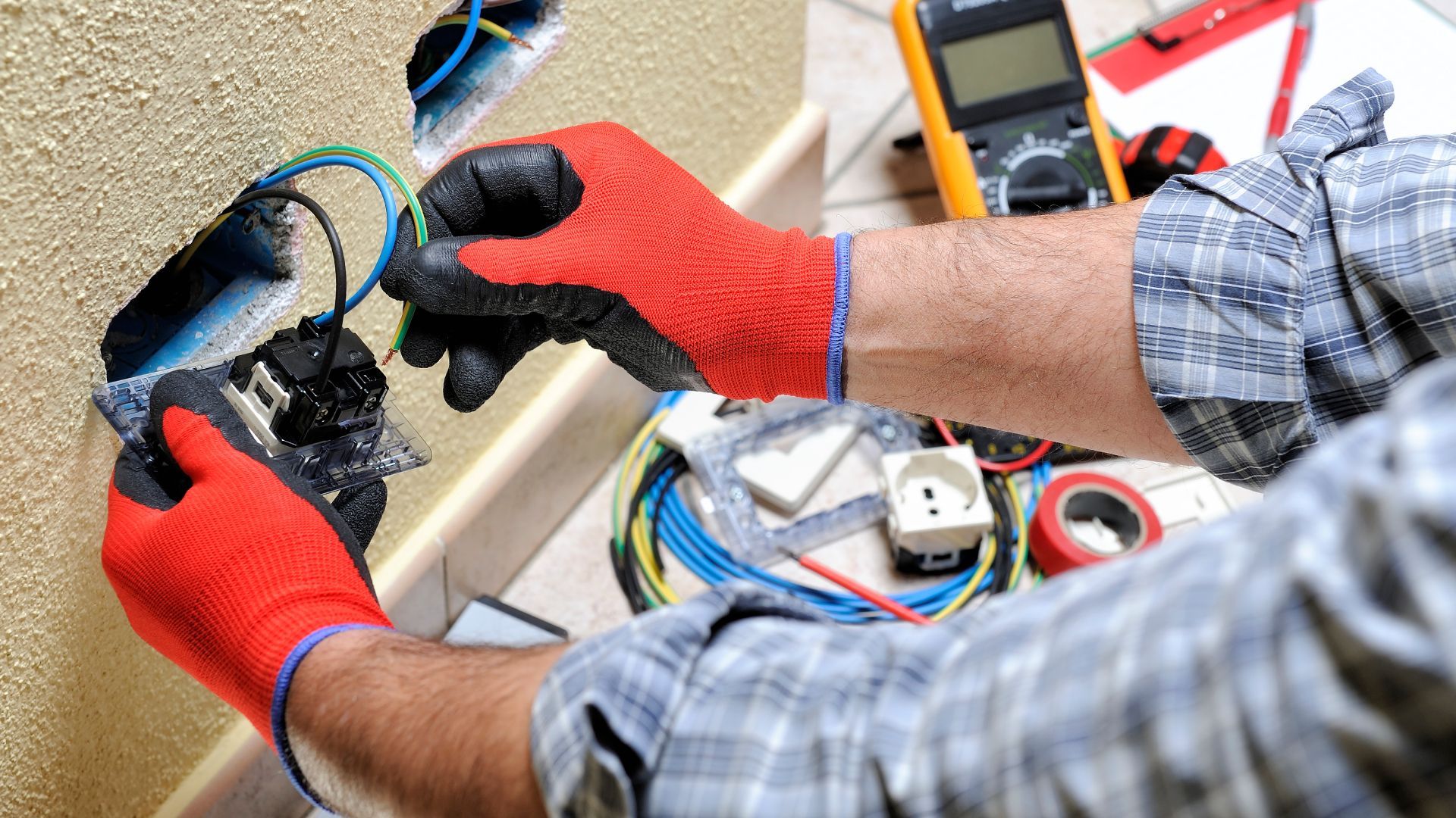 A man wearing red gloves is working on an electrical outlet.