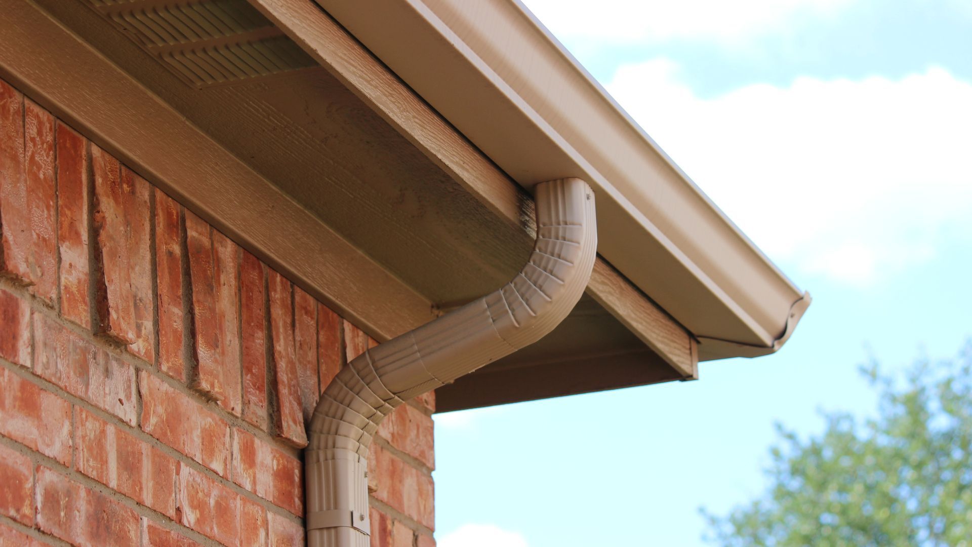 A close up of a gutter on the side of a brick house.