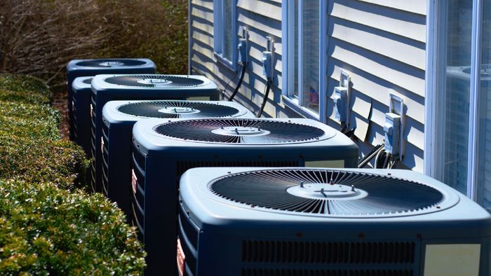 A row of air conditioners are lined up in front of a house.