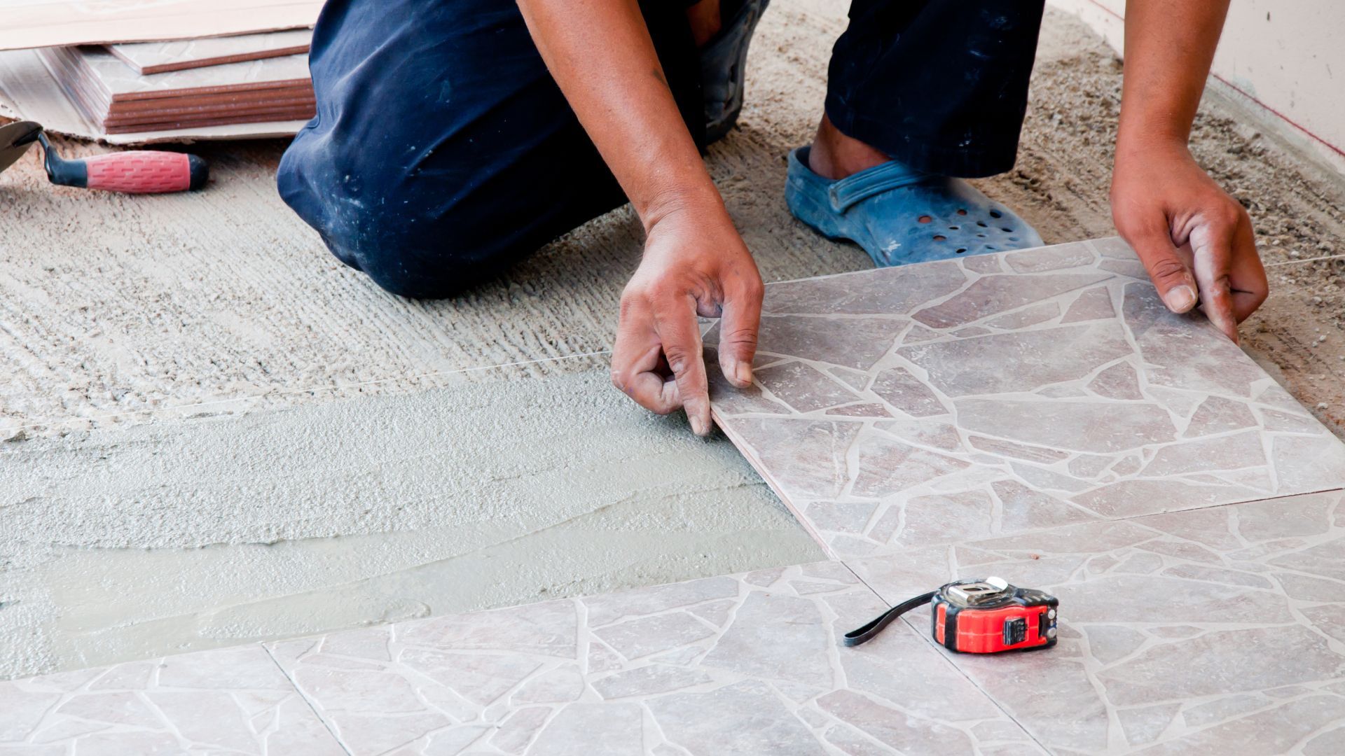 A man is kneeling down to install a tile floor.