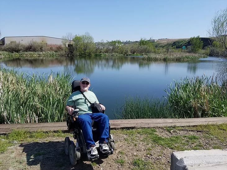 Person in a wheelchair by a calm lake on a sunny day.