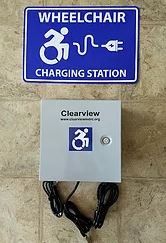 Blue sign: wheelchair charging station above a gray box with charger cables.