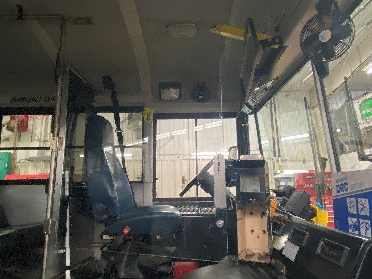 Interior of a bus driver's seat. Steering wheel, control panel, driver's seat, and view of the outside through the windshield.