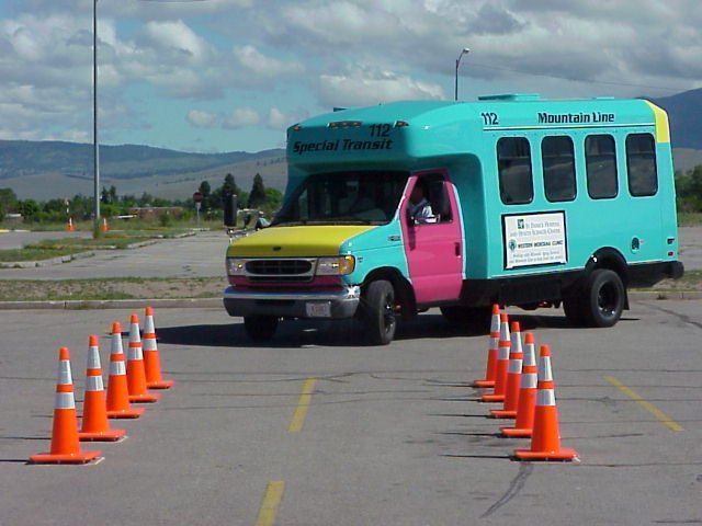 A colorful bus driving through orange traffic cones in a parking lot.
