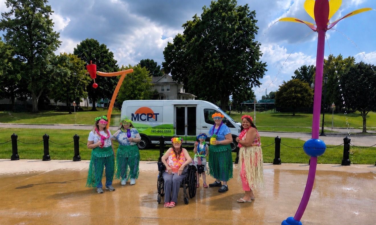 Riders in Hawaiian clothes at splash park near bus