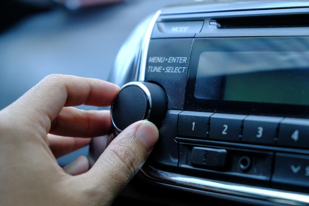 Hand turning a radio dial in a car, adjusting the volume or station.