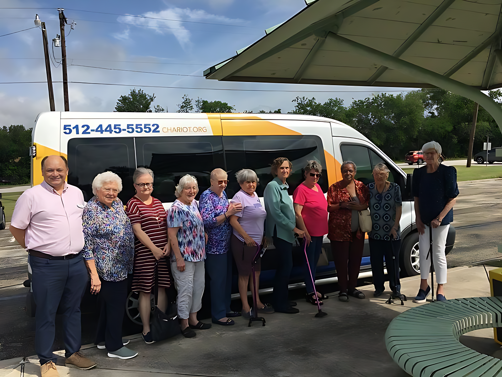 Group of seniors standing next to a transport van. Sunny day. Some use canes. Phone number on van.