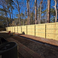 Wooden privacy fence along a backyard driveway under clear blue sky, with tire and brick path in foreground
