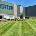Modern office building with green lawn, landscaped flower beds, and parked vehicles under clear skies