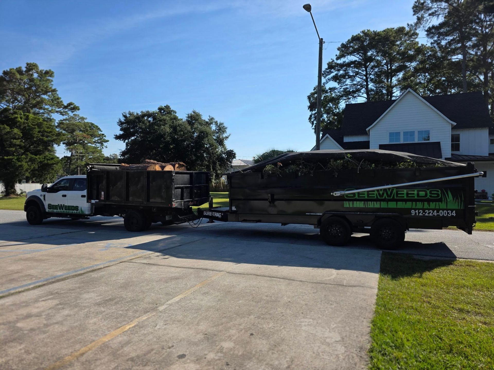 White truck towing a large black trailer parked on a driveway beside a house on a sunny day