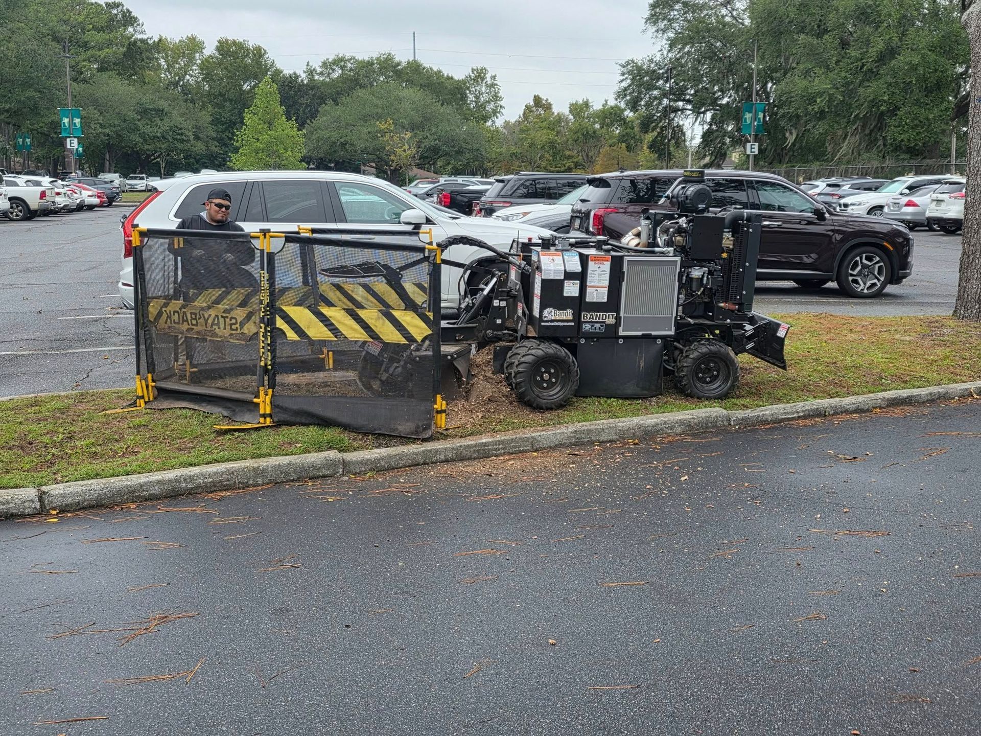 Two utility carts with yellow-black barriers in a wet parking lot, with trees and parked cars behind.