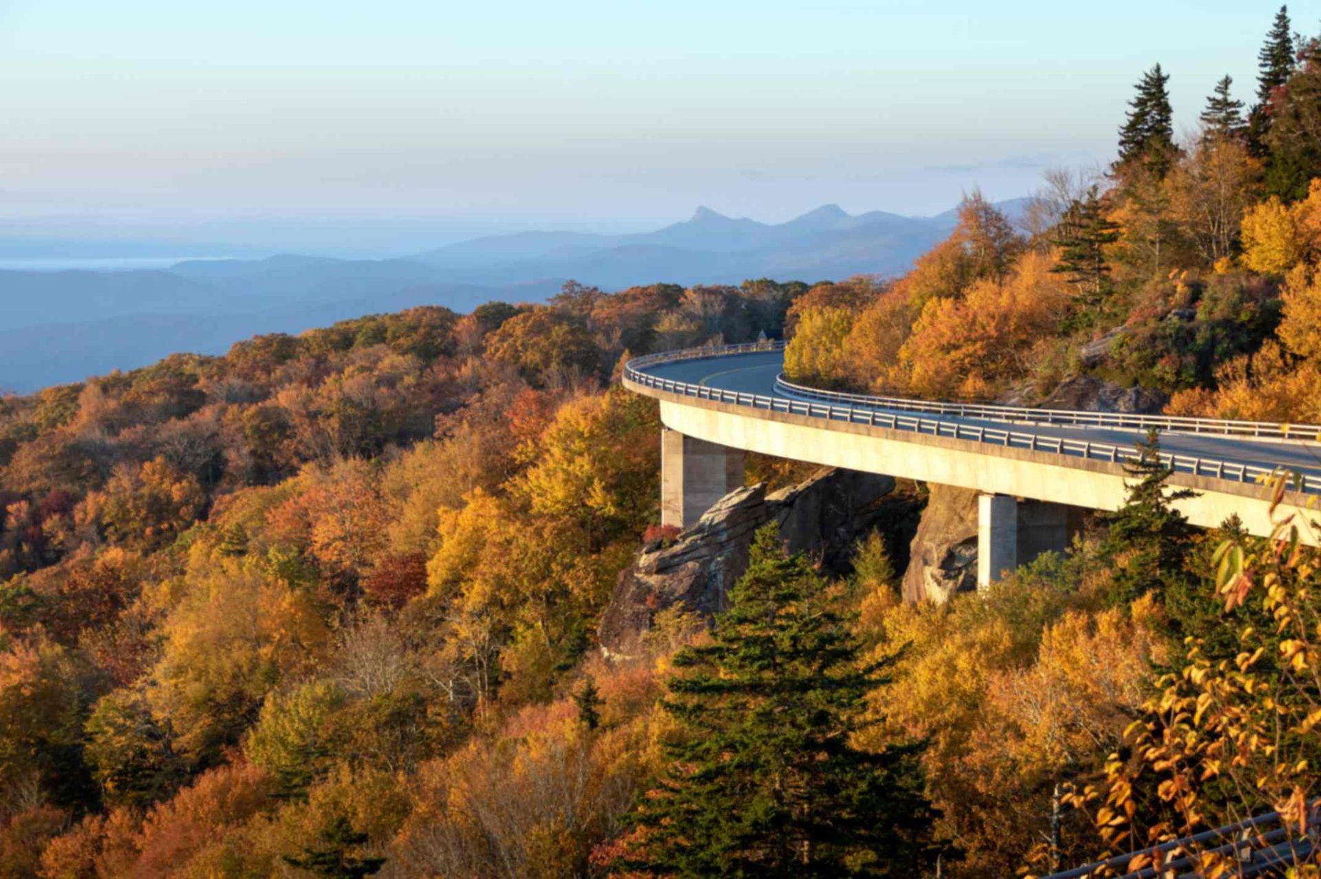 Scenic mountain road bridge above autumn forest, with distant blue mountains under a clear sky