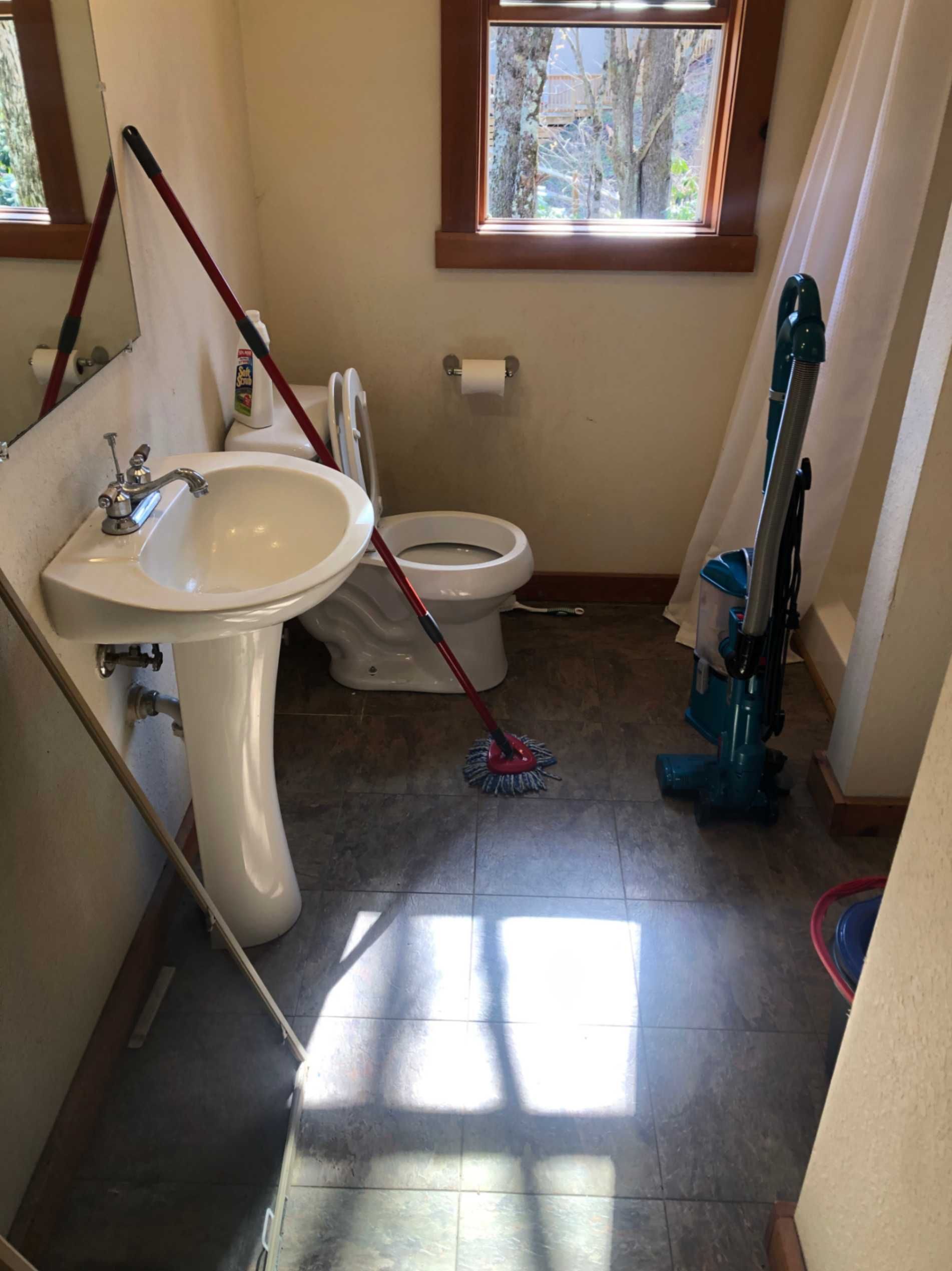 Small bathroom with sink, toilet, mop, and vacuum cleaner on a tiled floor.