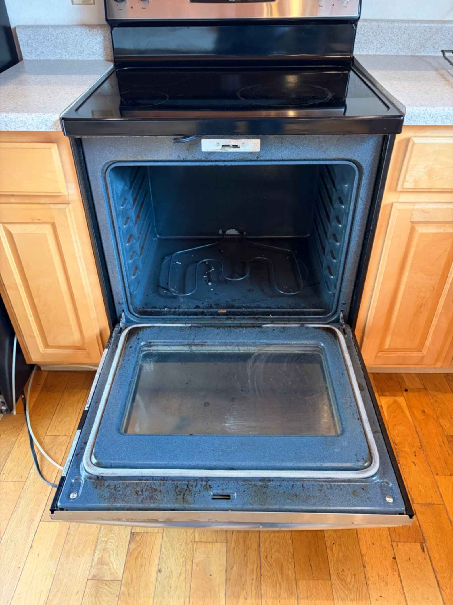 Open oven door on a black stove in a kitchen with wooden cabinets.