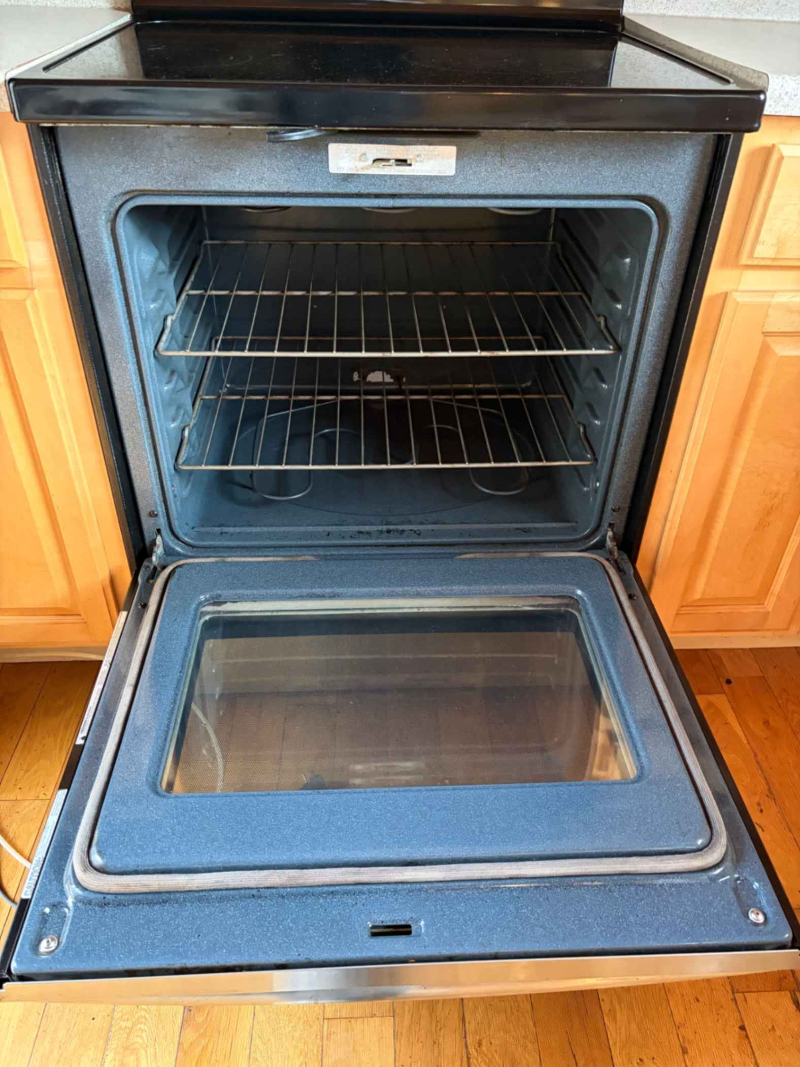 Open oven door with racks inside and a glass viewing window, surrounded by wood cabinets.