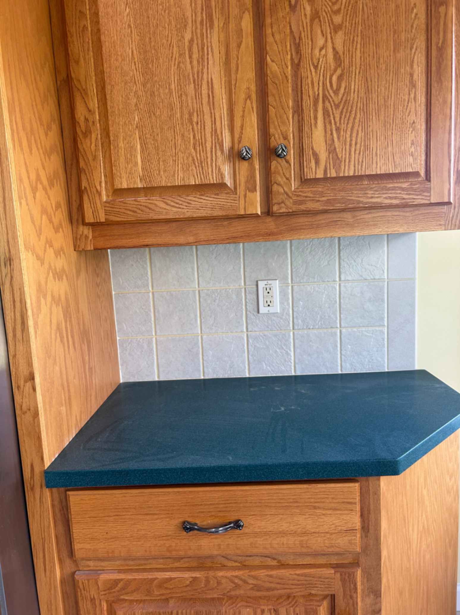 Corner kitchen counter with teal countertop, wooden cabinets, and tiled backsplash