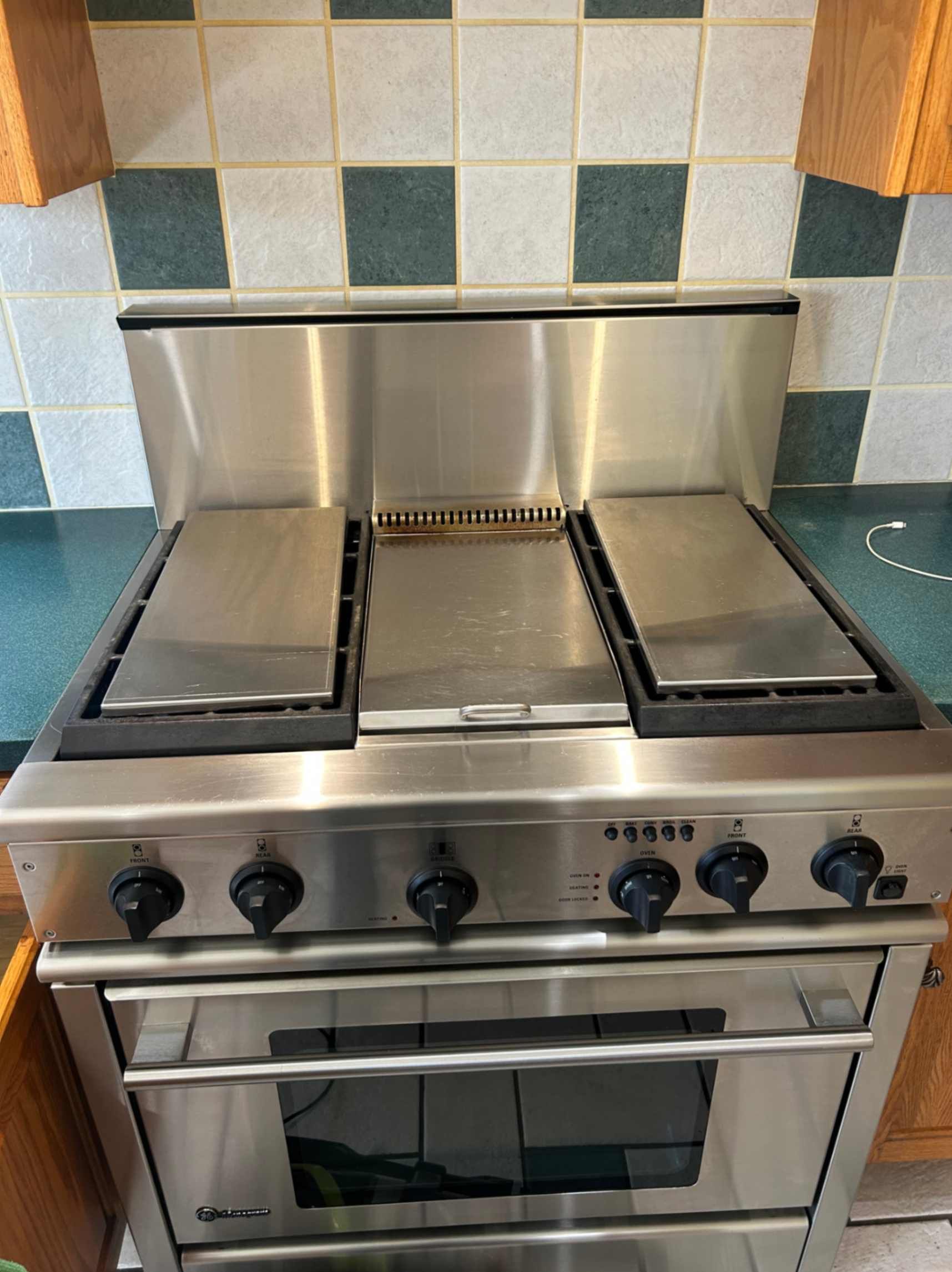 Stainless steel gas range with four burners and oven in a tiled kitchen nook