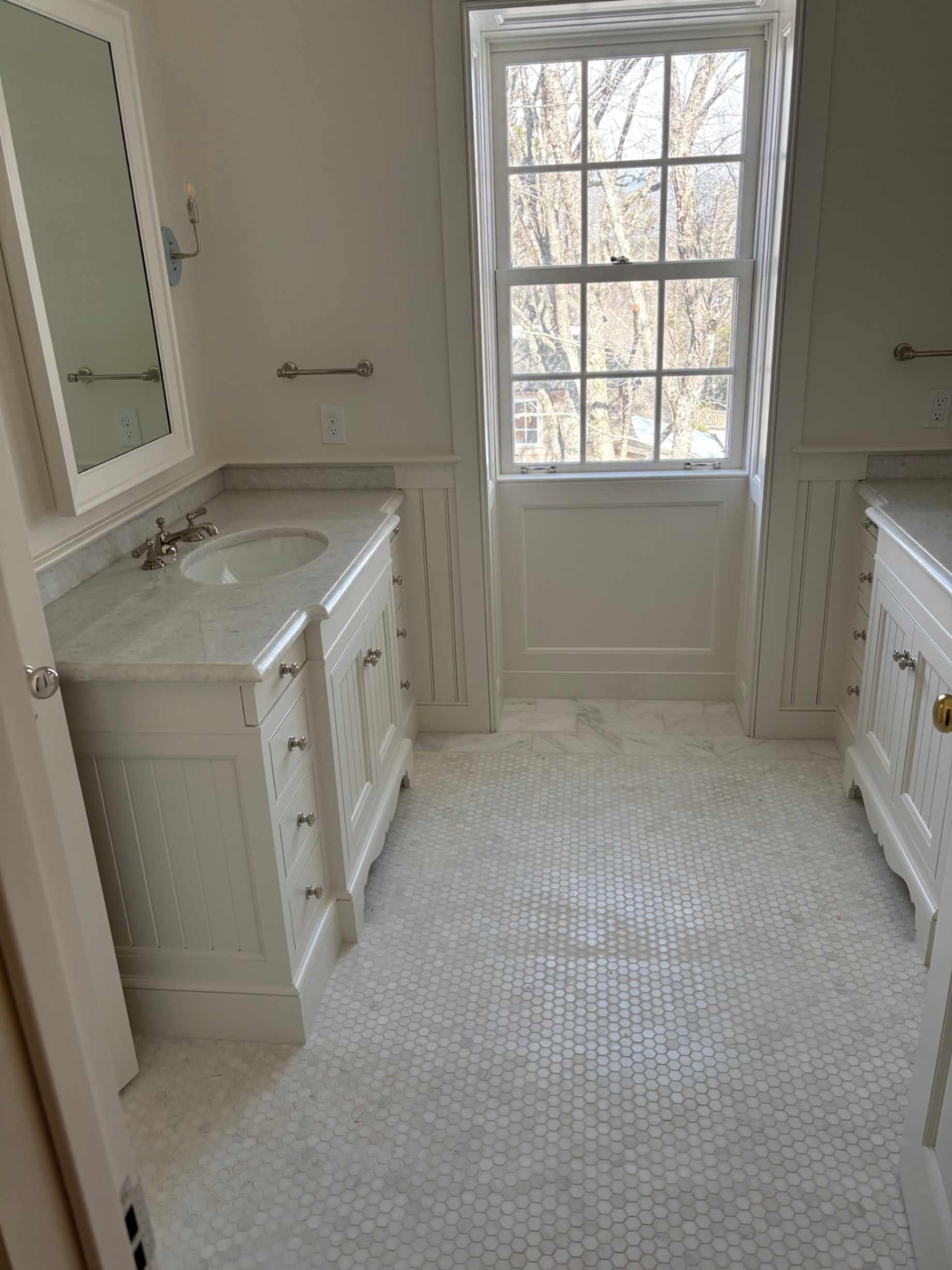 Bathroom vanity with round mirror, white sink, black countertop, wood wall, and hanging towel organizer