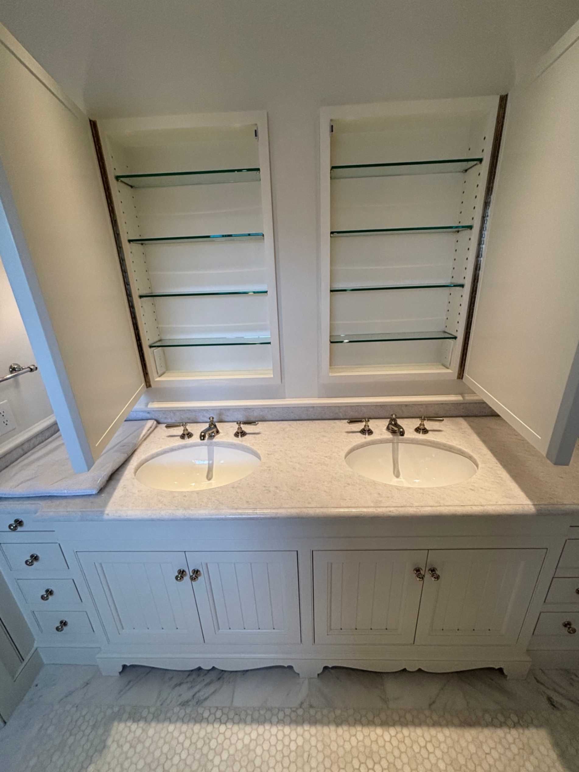 Double vanity bathroom sink with white cabinetry, large mirror, and glass shelves built into the wall