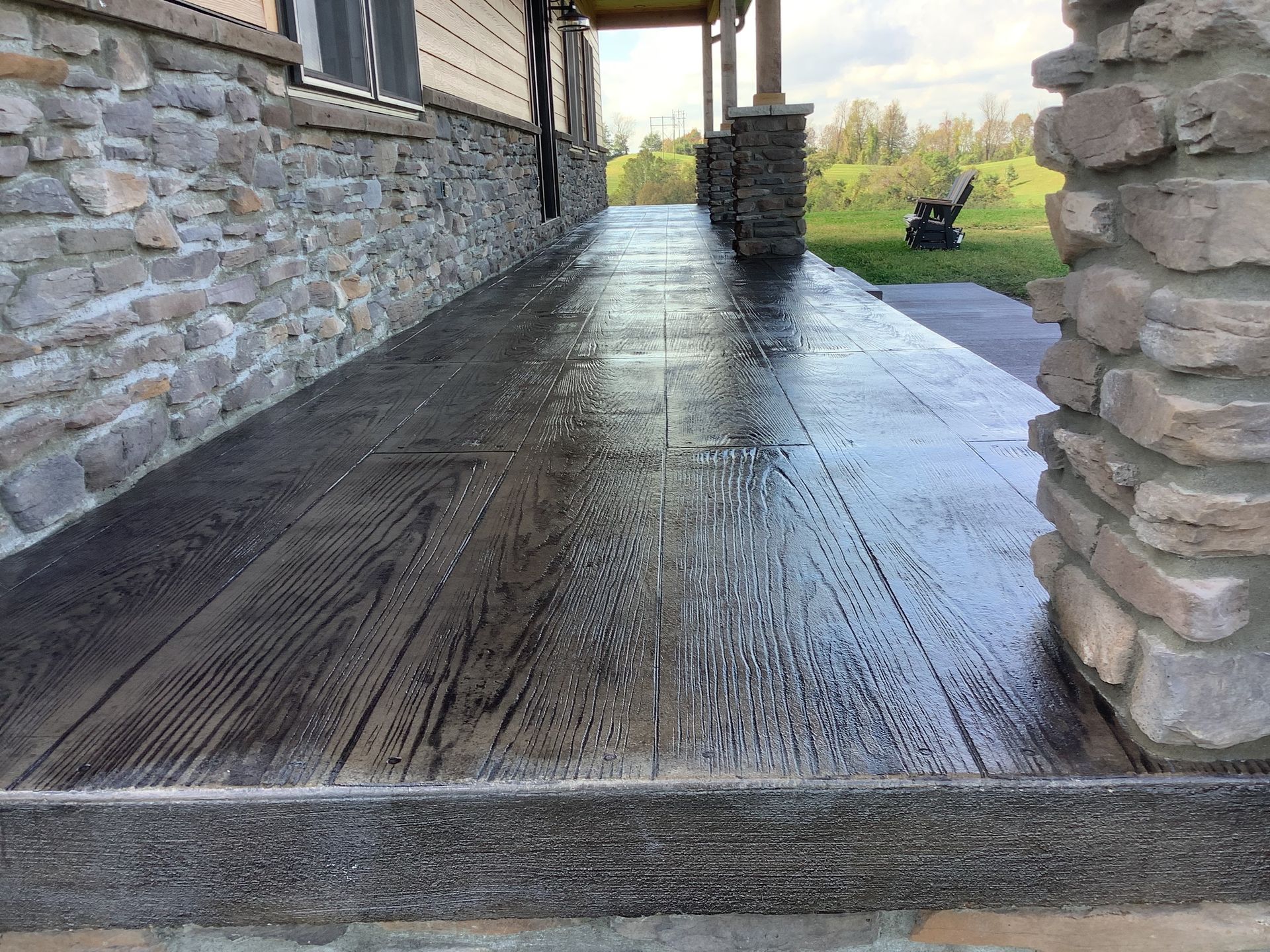Wood-textured concrete porch with stone accents, wet and reflecting light, part of a house.