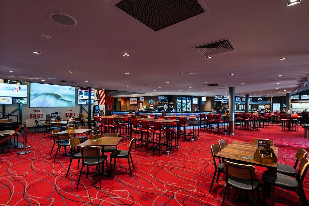 A sports bar with red carpet, tables, chairs, a bar, and multiple TVs showing games.