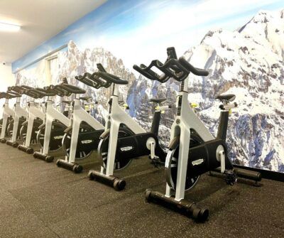 Spin bikes in a row at a gym, in front of a mountain mural.