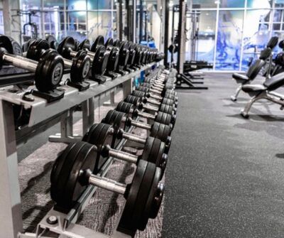 Rows of dumbbells on a rack in a gym, with benches in the background.