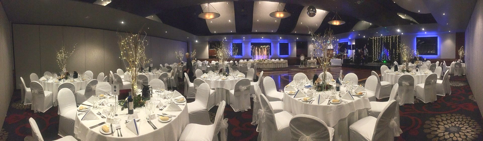 A banquet hall set up with round tables covered in white linens and chairs, and centerpieces ready for an event.