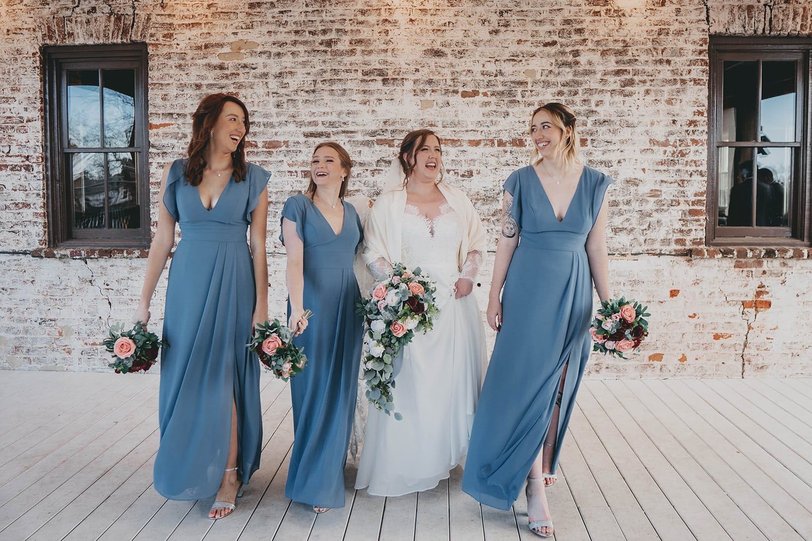 A bride and her bridesmaids are walking in front of a brick building.
