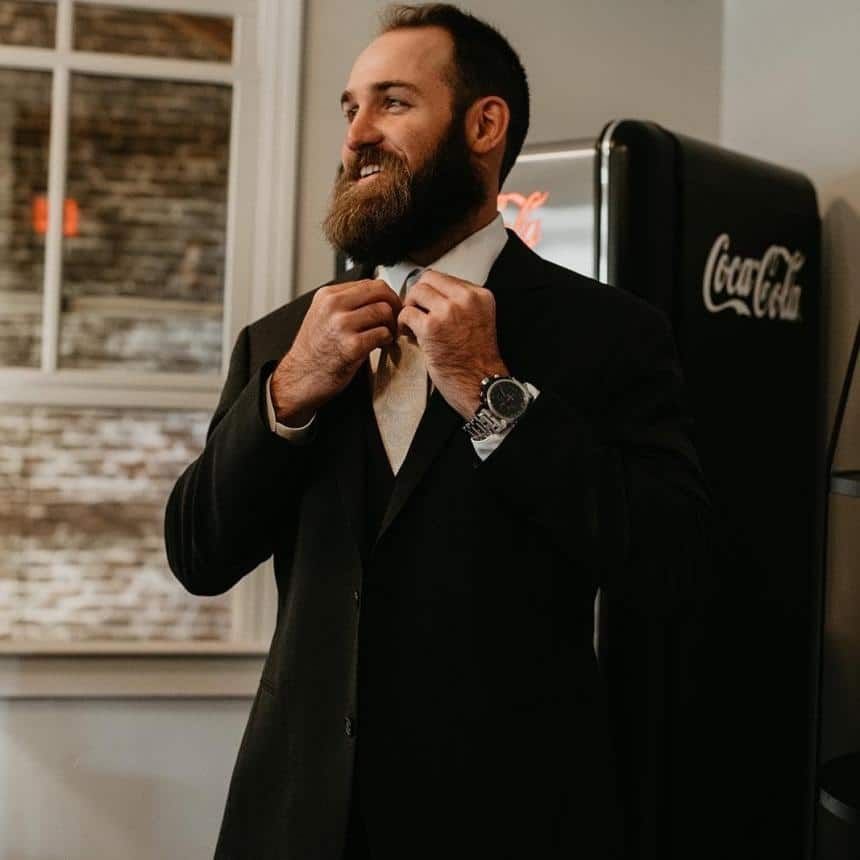 A man in a suit and tie is adjusting his tie in front of a coca cola refrigerator.